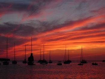 Silhouette sailboats sailing on sea against orange sky