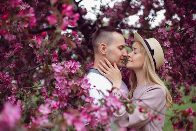 Portrait man and a woman in love stand by a blooming pink cherry tree in summer