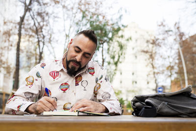 Bearded man sitting outdoors while working over a wooden table