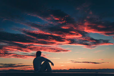 Rear view of silhouette man sitting against sky during sunset