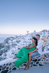 Young couple sitting on land by sea against clear sky