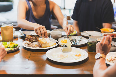 Woman eating fried eggs breakfast with friends on wooden table.
