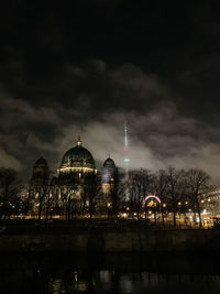 Illuminated building by river against sky at night