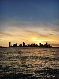 Silhouette buildings by sea against sky during sunset