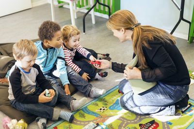 Full length of teacher giving toys to children