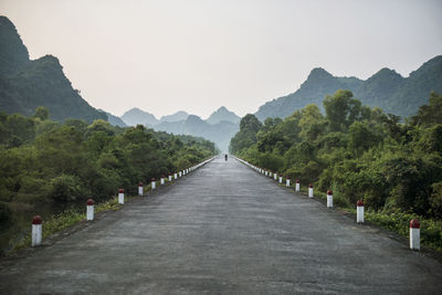 Empty road leading towards mountains against clear sky during foggy weather