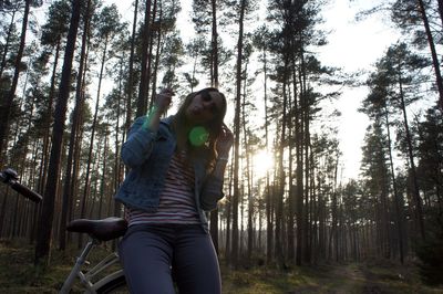 Portrait of woman making face while sitting on bicycle against trees at forest