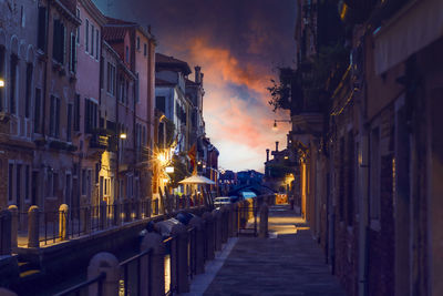 Illuminated street amidst buildings against sky at night