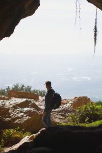 Man standing on rock looking at mountain against sky