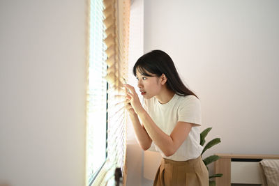 Side view of young woman standing against wall