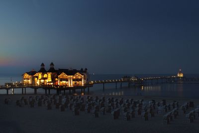 Illuminated buildings by sea against sky at night