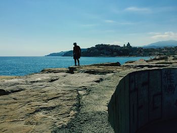 Man standing on retaining wall by sea against clear sky