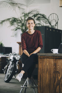 Portrait of smiling creative businesswoman sitting at kitchen island in office