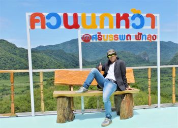 Portrait of man sitting on wooden seat against landscape