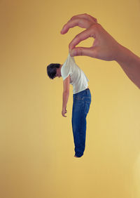 Side view of young man standing against yellow background