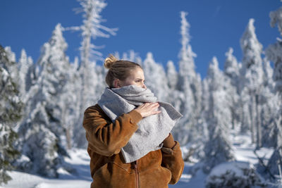 Young woman wearing warm clothing while looking away against trees during winter