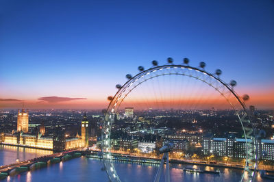 Illuminated ferris wheel in city against clear sky