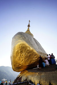 People praying by rocks against clear blue sky