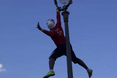 Low angle view of man with ball against clear blue sky