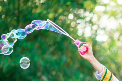 Close-up of hand making bubbles against trees