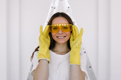 Portrait of a smiling woman painter designer in yellow safety glasses and gloves doing home repairs