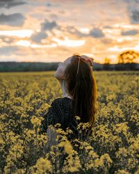 Woman standing amidst yellow flowers on field during sunset