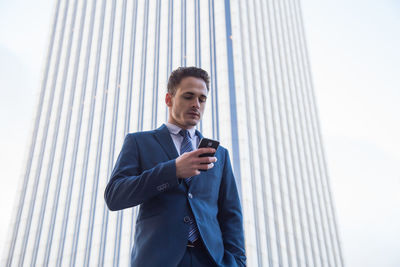 Low angle view of businessman using phone against wall