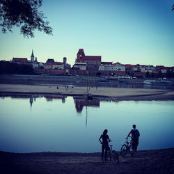 People on lake by buildings against clear sky