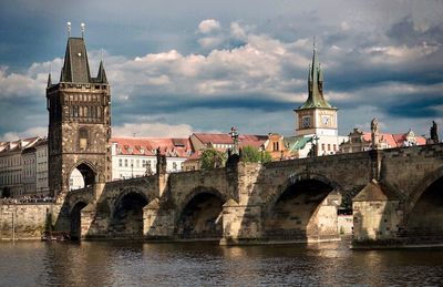 Arch bridge over river by buildings against sky