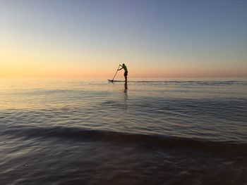 Silhouette man paddleboarding in sea against clear sky