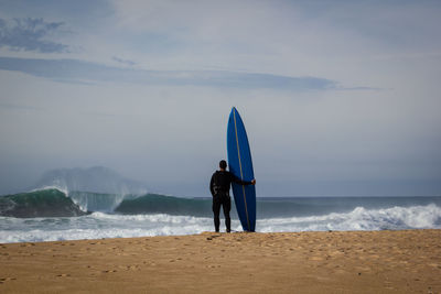 Rear view of men standing at beach against sky