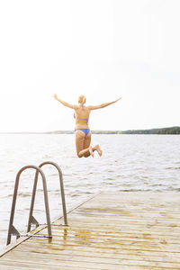 Rear view of woman with arms outstretched jumping into lake