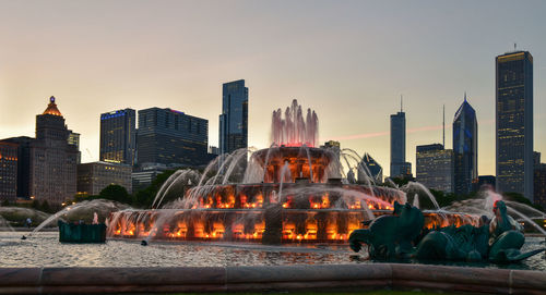 Illuminated buckingham fountain against skyscrapers in city at dusk