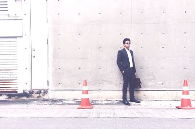 Businessman standing with briefcase amidst traffic cones against concrete wall