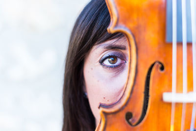 Close-up portrait of young woman hiding behind violin