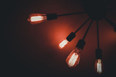 Low angle view of illuminated light bulbs hanging from ceiling in darkroom