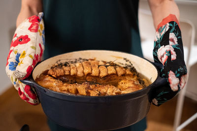 Woman holding pot-roast with colorful mittens.