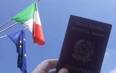 Low angle view of hand holding flag against blue sky