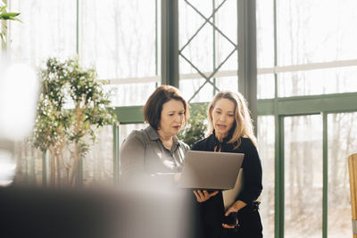 Serious businesswomen planning over laptop while standing in office corridor