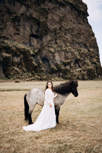 Woman with horse standing on field against rock formation
