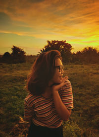 Beautiful woman standing on field against sky during sunset