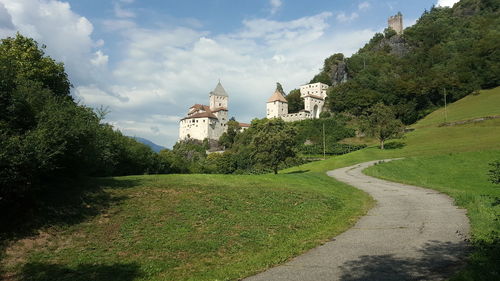 Footpath amidst trees and buildings against sky