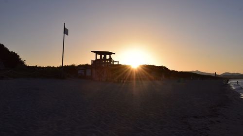 Silhouette beach against clear sky during sunset