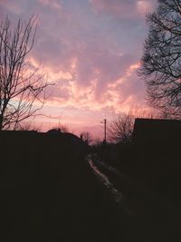 Silhouette bare trees by road against sky during sunset