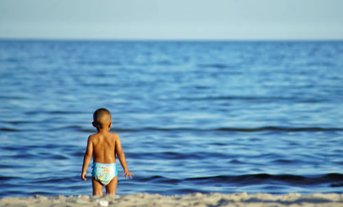 Rear view of shirtless boy standing at beach