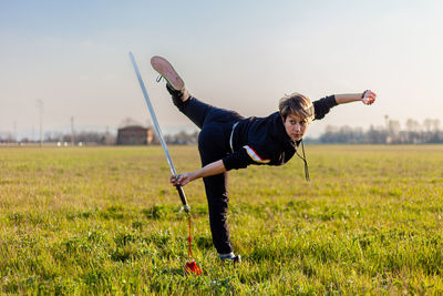 Caucasian young woman practicing wushu martial art on a green meadow with a sword