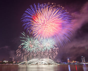 Low angle view of firework display over river against sky