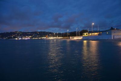 Illuminated city by river against sky at night