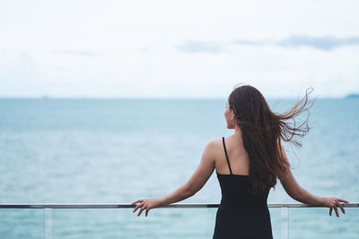 Woman standing at sea shore against sky