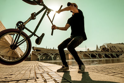 Man with bicycle against sky in city